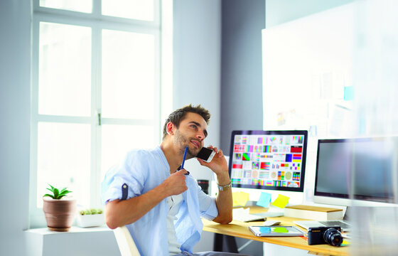 Portrait of young designer sitting at graphic studio in front of laptop and computer while working online.