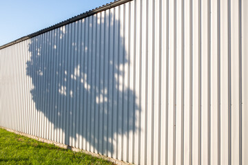 metal facade of a modern industrial building in the sun with shadow of a tree