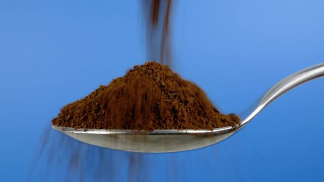 Ground coffee falling on a spoon. Closeup view on a blue background