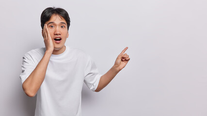 Horizontal shot of impressed Japanese man with short dark hair points towards open space urging you...