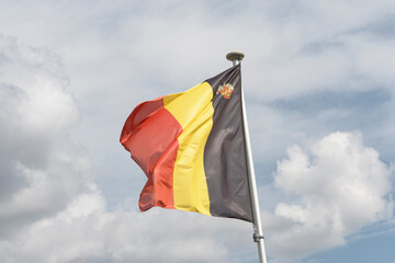 National flag of the Kingdom of Belgium against the background of clouds in the sky. Belgian National Day.
