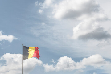 Belgian National Day. The national flag of the Kingdom of Belgium against the background of clouds in the sky. copy space