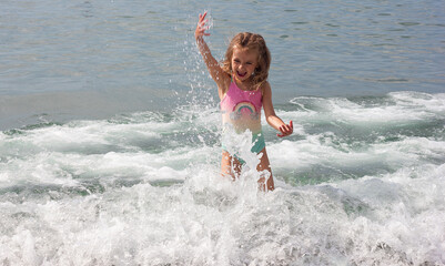 Beautiful happy little girl playing in the waves and splashes on the sea