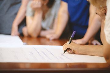 A woman writes with a marker on a paper canvas at the table.
