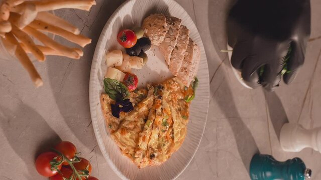 Chef hand serving omelet with aragula. Omelet with cherry tomatoes cheese olives and grain bread on the table with cup of coffee. Breakfast concept. Vertical shot