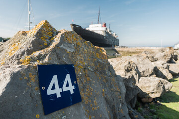 Blue number placard on a rock with a boat in the background, texture and travel concept illustration.