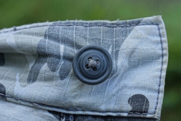 one large black plastic button on a gray fabric on clothes on a green background