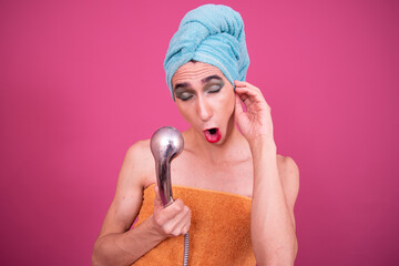Funny drag queen poses in the studio on a pink background to have fun, sing and take a selfie.
