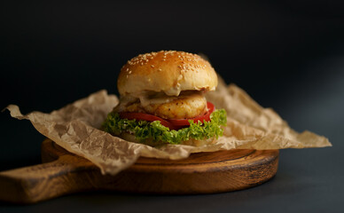 Close-up of a delicious fresh homemade burger with lettuce, cheese, onion and tomato on a rustic wooden board on a dark background