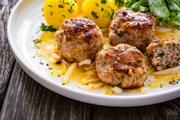 Seared pork meatballs with fried onion, boiled potatoes and lettuce in cream sauce on wooden table
