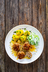Seared pork meatballs with fried onion, boiled potatoes and lettuce in cream sauce on wooden table
