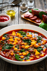 Delicious Spanish stew - chickpeas, spinach, seared chorizo, potatoes, tomatoes and broth on wooden table
