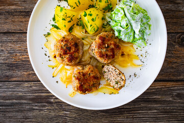 Seared pork meatballs with fried onion, boiled potatoes and lettuce in cream sauce on wooden table
