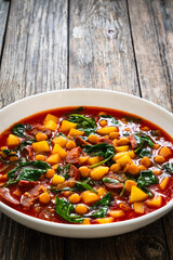 Delicious Spanish stew - chickpeas, spinach, seared chorizo, potatoes, tomatoes and broth on wooden table

