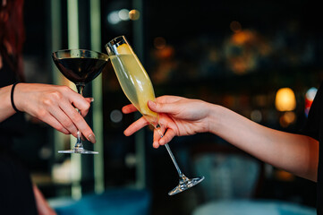hands of two women holding and clinking glasses cocktails in restaurant