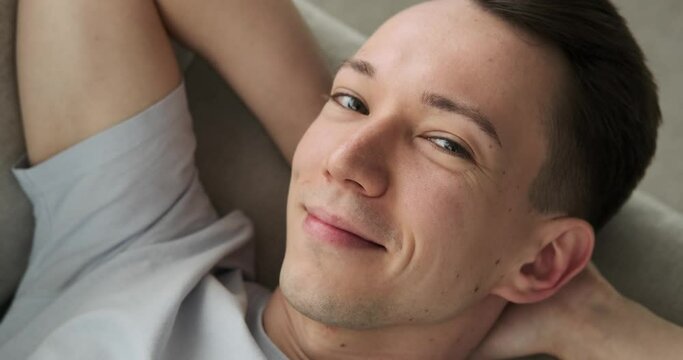 a Caucasian man lying comfortably on the couch, his eyes fixed on the camera, and a beaming smile adorning his face. Showing pure happiness and contentment.