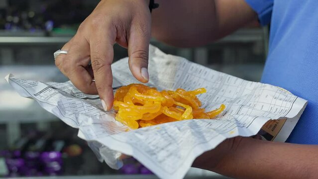 Closeup of a man holding and eating jalebis in a news paper at a roadside shop