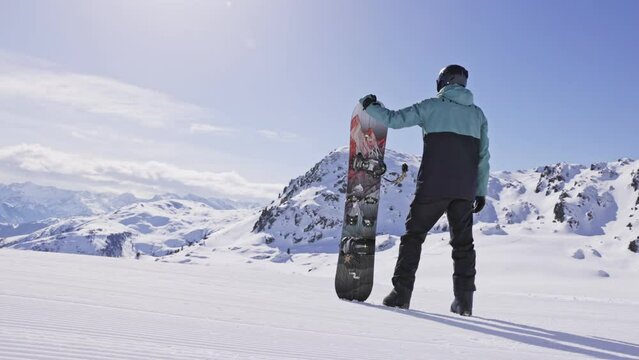 Slow motion of snowboarder looking at mountains. 4K skiing footage, one man snowboarder staying on ski slope on sunny winter vacation day with clear blue sky in European alps mountains, Austria.