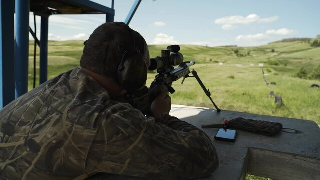 A shooter in camouflage uniform shoots at a target with a sniper rifle