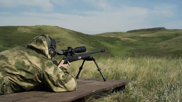 The shooter in camouflage takes aim and shoots at the target with a rifle