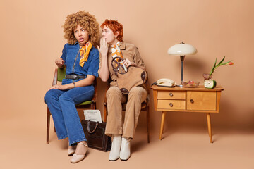 Women friends or colleagues wearing vintage outfits whisper secret and gossip between each other surrounded by classic retro furniture leaving viewers captivated by allure of nostalgia sit on chairs