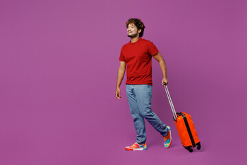 Traveler sideways Indian man wear red t-shirt casual clothes hold bag walk go isolated on plain purple background Tourist travel abroad in free spare time rest getaway Air flight trip journey concept