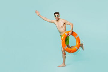 Full body young man wear green shorts swimsuit relax near hotel pool hold in hand lifebuoy run fast hurry up raise up hands isolated on plain blue background. Summer vacation sea rest sun tan concept. - Powered by Adobe