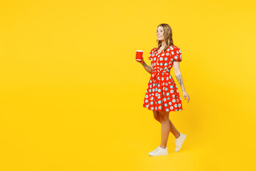 Full body young smiling caucasian woman wear red dress casual clothes hold takeaway delivery craft paper brown cup coffee to go isolated on plain yellow background studio portrait. Lifestyle concept.