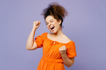 Young latin woman she wearing orange blouse casual clothes doing winner gesture celebrate clenching fists say yes isolated on plain pastel light purple background studio portrait. Lifestyle concept.