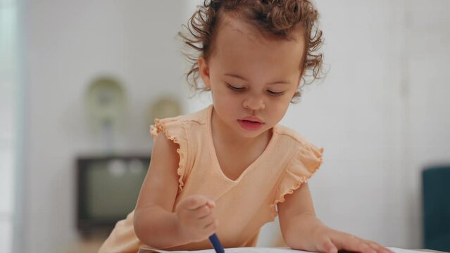 Little cute girl stand alone drawing and coloring with crayons in paper on table in living room at home. Learning of childhood.