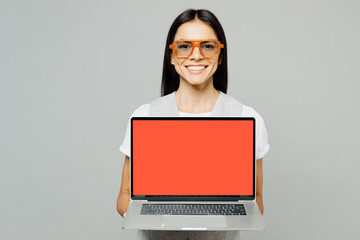 Young latin IT woman she wear white t-shirt gray vest glasses hold use work on laptop pc computer with blank screen workspace area isolated on plain grey background studio portrait. Lifestyle concept.