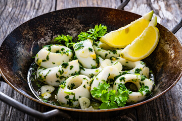 Fried calamari rings with garlic, lemon and parsley in pan on wooden table

