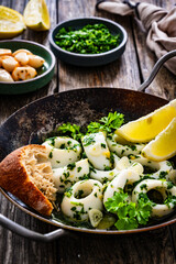Fried calamari rings with garlic, lemon and parsley in pan on wooden table
