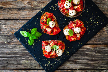 Tasty sandwiches - toasted bread with mozzarella balls cheese, tomatoes and basil leaves on wooden table
