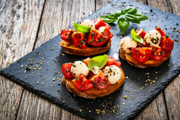 Tasty sandwiches - toasted bread with mozzarella balls cheese, tomatoes and basil leaves on wooden table
