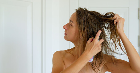 Naklejka premium Young woman in towel near mirror using hair spray in bedroom