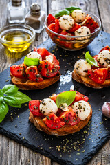 Tasty sandwiches - toasted bread with mozzarella balls cheese, tomatoes and basil leaves on wooden table
