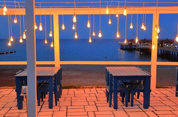 Tavern by the sea with many lightbulbs and pier in the evening.