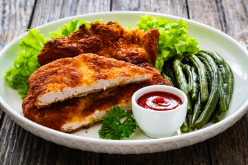 Breaded fried pork chop with cooked green beans on wooden table
