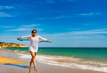 Fototapeta na wymiar Beautiful woman walking on sunny beach holding shawl 