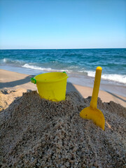 Fototapeta na wymiar a yellow bucket and shovel in the sand on the beach for children to play sand castles, you can also see the Mediterranean Sea and the beach
