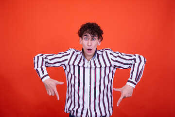 Young attractive emotional guy posing in the studio on an orange background.