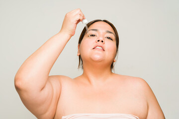 Naklejka premium Fat hispanic woman using hyaluronic acid oil or serum