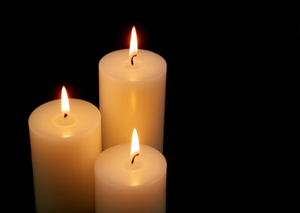 Fototapeta na wymiar White candles with different size burning on black background with space for text.