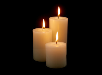 Fototapeta na wymiar Three white candles with different size burning on black background.