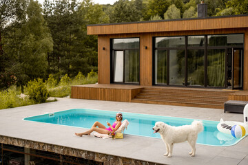 Woman with her dog resting at luxury wooden house with a swimming pool, wide view on property