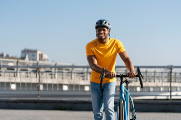 Fototapeta na wymiar Portrait of smiling African rider wearing protective helmet rides bicycle on urban street outdoors