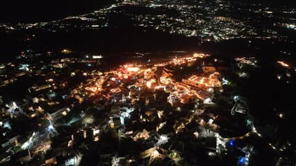 Cinematic 4k aerial video of the Greek town of Pyrgos being illuminated by rooftop candles during orthodox easter good friday celebrations on the island of Santorini
