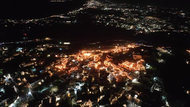 Cinematic 4k aerial video of the Greek town of Pyrgos being illuminated by rooftop candles during orthodox easter good friday celebrations on the island of Santorini