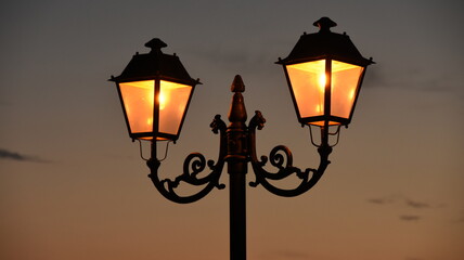 Old ornamented Street Lamp Gas light lantern retro 1800 style warm illuminated  at dawn night town - obrazy, fototapety, plakaty